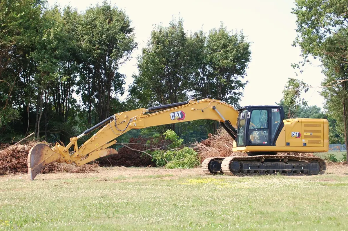 An excavator clearing scrub and trees from a grassy site