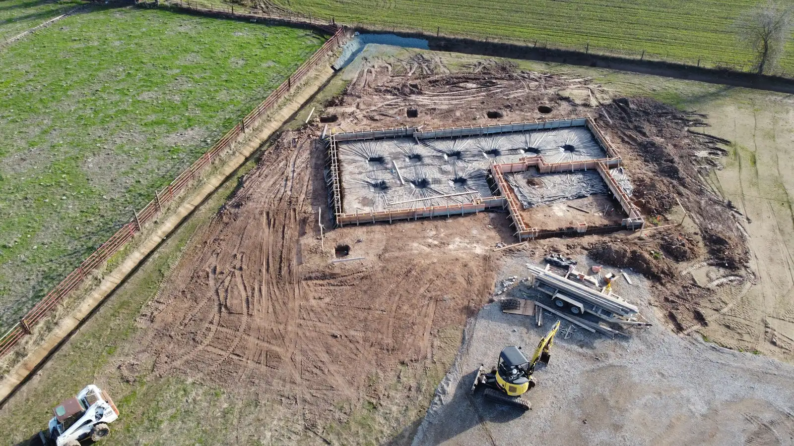 Foundations for a new building seen from above, with a mini digger on the site