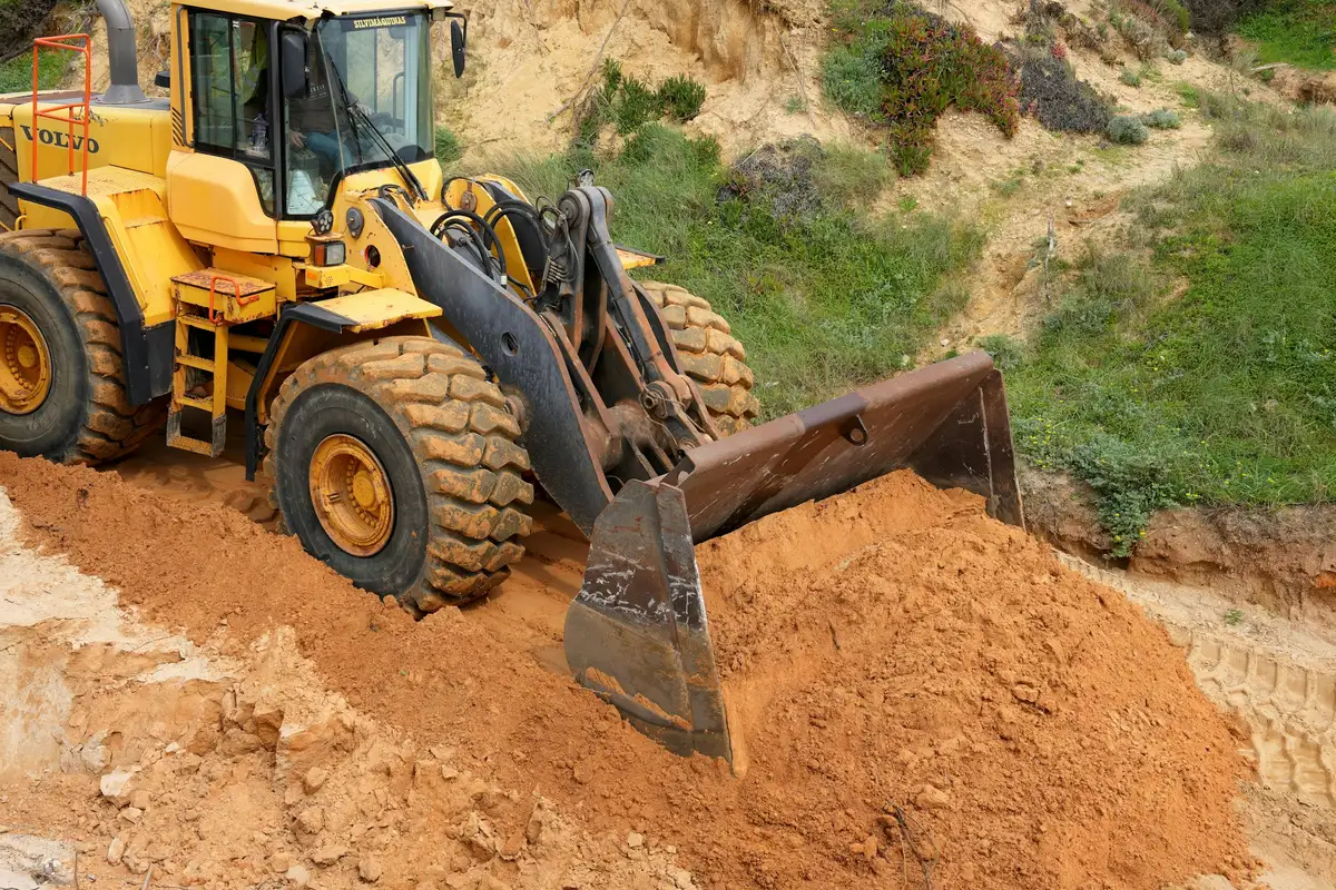 A wheeled loader pushing a pile of sandy soil on a sloping site