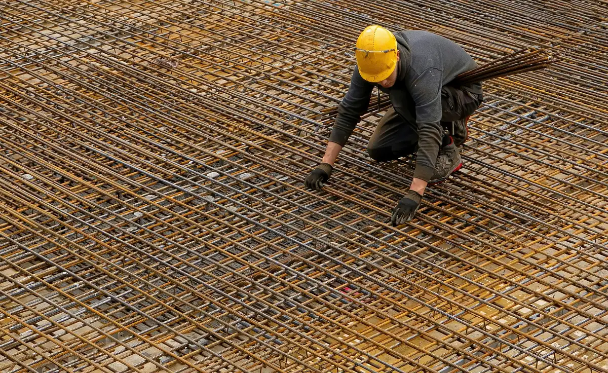 A worker in a hard hat laying steel reinforcement mesh for a slab