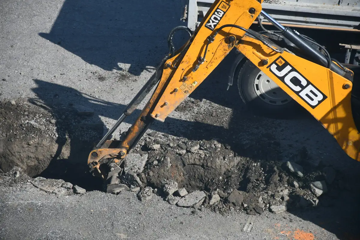 A backhoe loader digging a trench through a road surface